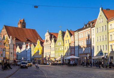 Landshut, Almanya - 19 Mart 2025: Renkli binalar, açık kafeler ve yürüyen insanlarla dolu tarihi Landshut kasabasında canlı bir sokak sahnesi. Gökyüzü açık ve mavi.