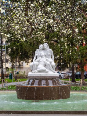 Innsbruck, Avusturya - 21 Mart 2025: Saliger Fraulein 'in beyaz mermer heykeli dairesel bir fıskiyenin üzerinde su jetleriyle oturuyordu. Çiçek açan ağaçlar, park dekorları, bahar atmosferi..