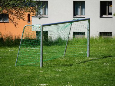 Yeşil ağlı bir futbol topu konut binalarının yakınındaki çimenli bir arazide duruyor..