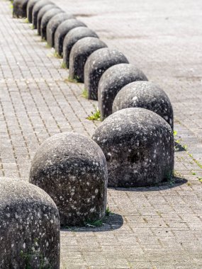 Asfaltlı bir yüzeyde bir sıra yuvarlak taş, eskimiş dokular ve yosun büyümesi sergiliyor. Sahne, minimalist bir şehir tasarım öğesini yakalıyor..