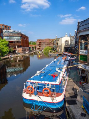 Londra, Birleşik Krallık - 28 Nisan 2025: Berrak mavi bir gökyüzü altında kentsel mimari ve yemyeşil ile çevrili durgun suda yansıyan demirlemiş bir tekneyle canlı bir Vekil kanalı sahnesi.