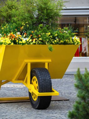 Renkli çiçekler ve yeşilliklerle dolu canlı sarı bir el arabası kaldırım taşlı bir caddeye kurulmuş. Sahne canlı ve cezbedici, gösterişli şehir bahçeleri..