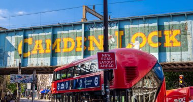 Londra, Birleşik Krallık - 28 Nisan 2025: Camden, Londra 'da canlı bir sokak sahnesi, ikonik Camden Lock demiryolu köprüsünün altından geçen kırmızı çift katlı bir otobüs.