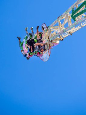 Maastricht, Hollanda - 12 Mayıs 2025: Açık mavi gökyüzüne karşı baş aşağı asılı süvarilerle heyecan verici bir lunapark gezisi. Turda renkli koltuklar ve dinamik bir yapı yer alıyor.