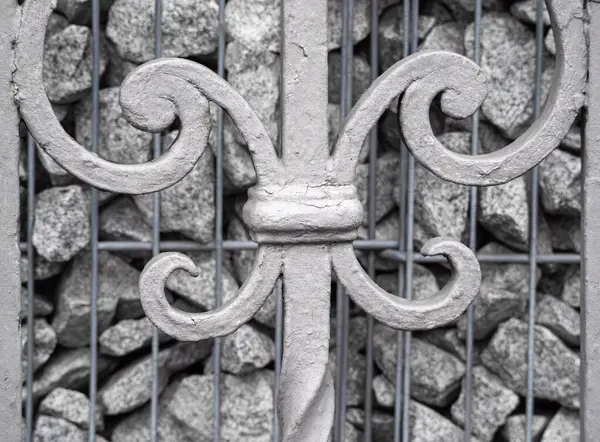 Gri taşlardan oluşan bir zemin üzerine kurulmuş karmaşık girdaplarla süslü gri bir metal kapı tasarımı..