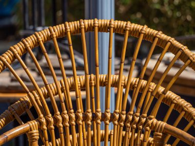 Çok güzel hazırlanmış bir sandalyenin yakın plan çekimi, karmaşık dokuma desenleri ve doğal ahşap tonları sergiliyor. Arkaplan özellikleri bulanık açık hava elementleri.