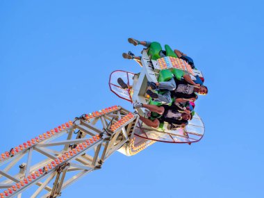 Maastricht, Hollanda - 12 Mayıs 2025: Açık mavi gökyüzüne, canlı renklere ve dinamik hareketlere karşı asılı, deneyimin tadını çıkaran insanlarla heyecan verici bir lunapark gezisi