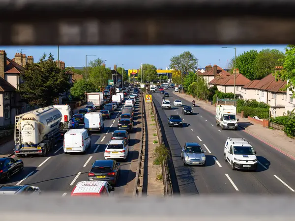 Londra, Birleşik Krallık - 28 Nisan 2025: Londra 'da trafik yoğun, arabalar ve kamyonlar da dahil olmak üzere karayolu bir medyan tarafından bölünmüş, evler cadde boyunca dizilmiş. Metal parmaklıklardan baktık..