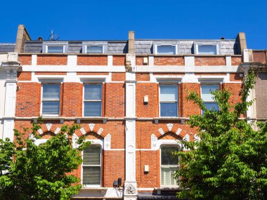 Londra, Birleşik Krallık - 28 Nisan 2025: Açık mavi gökyüzü altında beyaz aksanlı ve yurt pencereli Londra Hackney 'nin klasik tuğladan bir konağı.