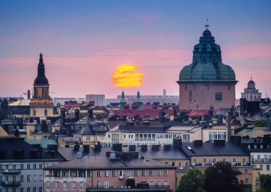 Stockholm şehrinin ufuk çizgisi üzerinde çarpıcı bir günbatımı, tarihi ve modern mimarinin bir karışımı. Güneş büyük ve turuncu..