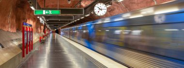 Stockholm, İsveç - 9 Haziran 2025 Stockholm Radhuset metro istasyonunun panoramasında hareket halindeki bulanık bir tren ve duvarda bir saat.