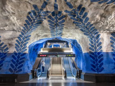 Stockholm, İsveç - 9 Haziran 2025 Stockholm 'deki T-Centralen metro istasyonu, eşsiz kaya oluşumları ve sanatsal mavi desenler. Dijital tabelalı bir yürüyen merdiven platforma çıkıyor..