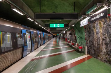 Stockholm, İsveç - 9 Haziran 2025 Stockholm 'de bulunan modern bir Kungstradgarden metro istasyonu, platformda bir tren, yeşil ve kırmızı tabela ve benzersiz bir kaya duvar tasarımı.