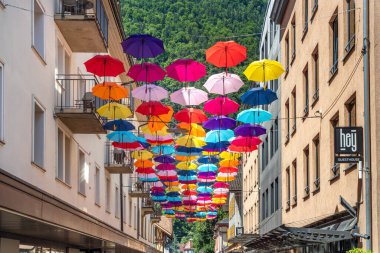 Interlaken, İsviçre - 17 Temmuz 2025: Interlaken 'de dar bir ara sokakta asılı renkli şemsiyelerin yer aldığı canlı bir sokak manzarası. Misafir evi tabelası.