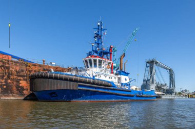 Hamburg, Almanya - 1 Temmuz 2025: Hamburg limanında büyük bir sanayi duvarının yanına bir römorkör yanaştı.