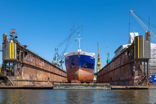 Гамбург, Германия - 1 июля 2025 года: Большой корабль по имени Иоганн в сухом доке в Гамбурге, окруженный промышленными кранами и машинами под ясным голубым небом.