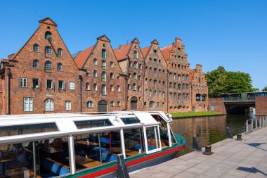 Lubeck, Almanya - 2 Temmuz 2025: Basamaklı tuğlalı tarihi binalar, açık mavi bir gökyüzünün altında, ön planda bir tur botu bulunan kanallar..