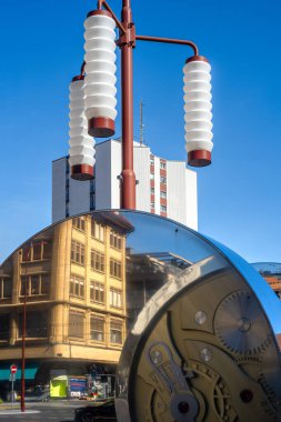 La Chaux-de-Fonds, İsviçre - 19 Eylül 2025: Silindirik cam gölgeli modern bir sokak lambası, tarihi bir binayı ve arka planda uzun bir yapıyı yansıtıyor, saat üretim endüstrisi