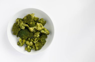 Freshly cooked broccoli in a white bowl on a white background.