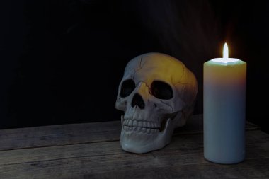 Eski bir masanın üzerindeki mumla aydınlatılmış kafatası.