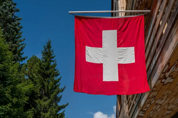 Swiss flag. Switzerland flag hanging on roof against blue sky. One red square flag with a white cross in the centre.