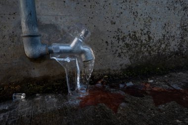 Su musluğunda çatlak var. Donmuş bir musluk ve kışın yere dökülen su..