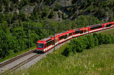 Grengiols, Valais Canton, İsviçre - 27 Mayıs 2023: İsviçre 'de ilkbaharda bir kırmızı tren ve beyaz tren raylardan geçiyor.