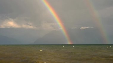 Suyun üstünde gökkuşağı. Cenevre Gölü manzarası, dağ ve dalgalar ve gökyüzünde çift gökkuşağı. Lozan, Vaud Canton, İsviçre. Gerçek zamanlı..
