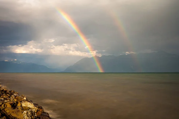 Rainbow over water. Landscape of lake Geneva, mountain and waves and double rainbows in the sky. Lausanne, Vaud Canton, Switzerland.