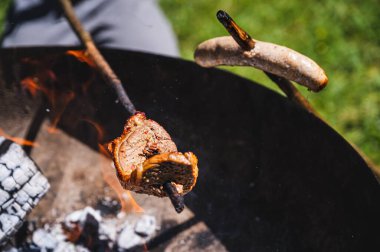 Barbekü yanıyor. İsviçre 'de kamp ateşinin üstünde sosis ve biftek ısıtılıyor. Lezzetli yemek..