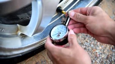  Adam arabayı kullanmadan önce lastik basıncını kontrol etmek için TIRE GAUGE kullanıyor.