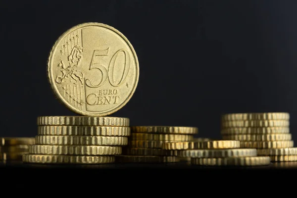 50 euro cents coin perched on top of other euro coins on a dark background