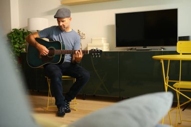 Evde oturan bir adam akustik gitarla akor çalmayı öğreniyor.