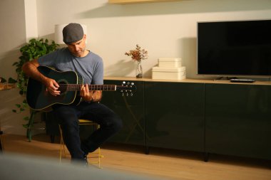 A man sitting at home learning to play a chord on acoustic guitar clipart