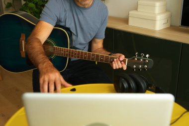 Bilgisayarın önünde oturmuş online müzik dersleri alan bir adam.