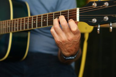 Evde akustik gitarda D akoru çalan bir adamın ellerinin yakın çekimi.
