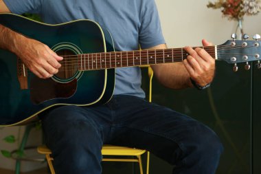 Evde akustik gitarda G akoru çalan bir adamın ellerinin yakın çekimi.