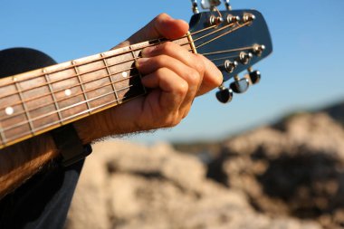 Akustik gitarla E akoru çalan bir adamın yakın çekimi.