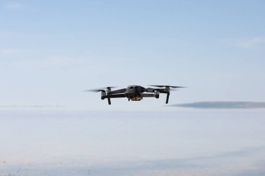 Dark gray unmanned drone quadcopter flying isolated over a body of water, soft focus