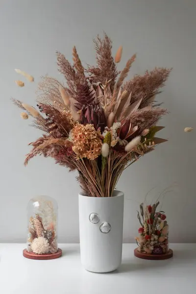 Kurumuş çiçeklerle dolu güzel bir buket ve beyaz masadaki vazoda kurumuş çiçekler. iç dekorasyon.