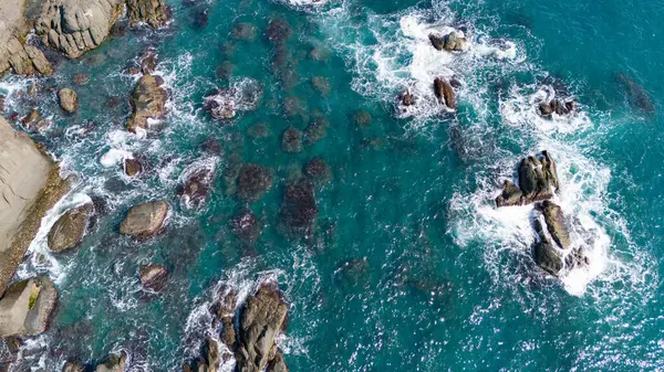 Açık mavi dalgalar kayaların arasında dalgalanıyor..