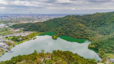 Meihu Gölü 'nün sakin yansımaları yemyeşil ve uzak şehir siluetinin ortasında