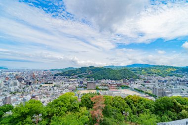 Arka planda dağlar olan panoramik şehir manzarası. Hareketli bir Japon şehrinin üzerinde dinamik bulutlar.