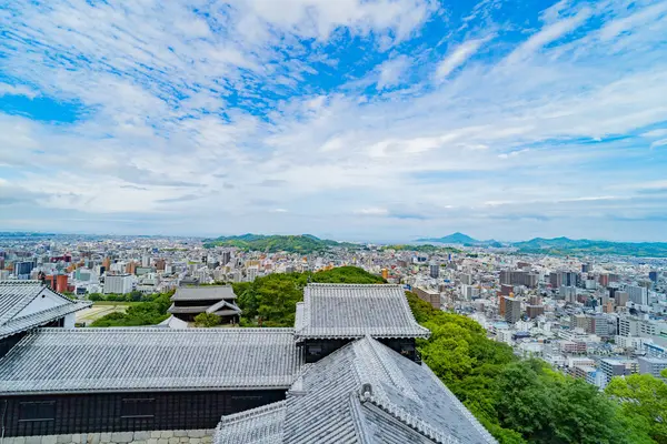 Geleneksel Japon şatosu çatıları genişleyen modern bir şehre bakıyor. Tarihi ve kentsel panorama.