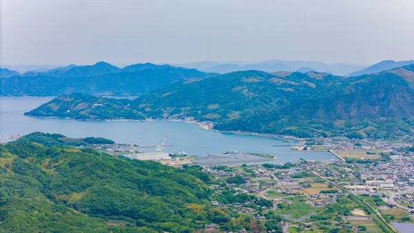 Yeşil arazilerin arasına yerleşmiş büyüleyici deniz kenarı topluluğu. Sakin sular, puslu zemin.