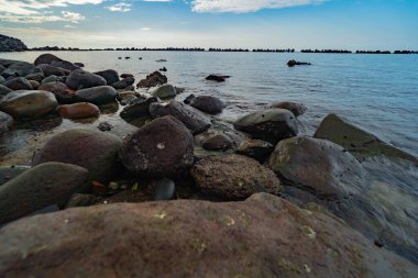 Yumuşak dalgaları ve parlayan akşam gökyüzü olan kayalık kıyı şeridine yakın..