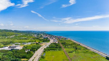 Tayvan 'ın batı kıyı şeridine ait bir hava manzarası. Yeşil tepeler ve kıyıya paralel uzanan demiryolu ve karayolu ile çevrili engin mavi deniz arasında bir kıyı kasabası var..