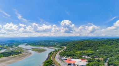 Sakin bir nehir boyunca uzanan dolambaçlı bir yol canlı mavi gökyüzünün ve dramatik yaz bulutlarının altında, manzaralı keşiflere davetiye çıkarıyor..