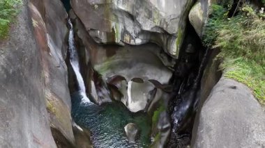 Doğal bir kaya oluşumunun havadan görünüşü kristal berraklığında bir havuz ve çağlayan şelaleler yemyeşil sularla çevrili.