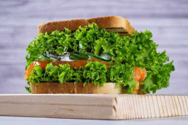 Taze somonlu sandviç, marul, salatalık ve sos açık renkli kesim tahtasında, açık arkaplanda. Ev yapımı. Sağlıklı yemek..  